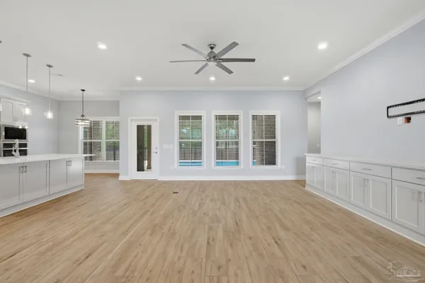 a view of an empty room with wooden floor and a kitchen