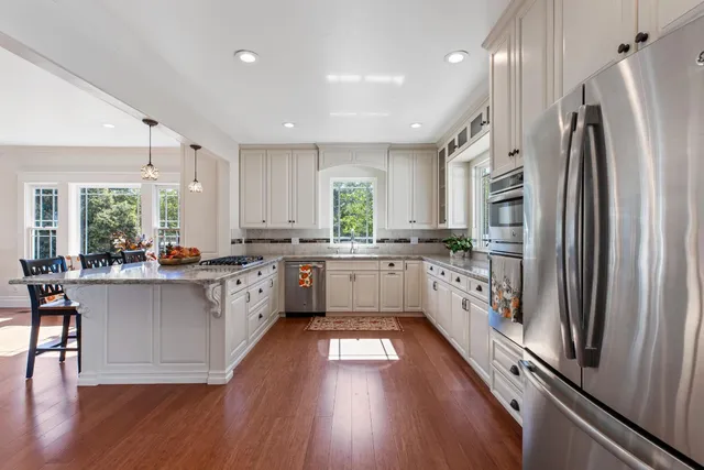 a kitchen with stainless steel appliances granite countertop a refrigerator a sink dishwasher a stove and white cabinets with wooden floor