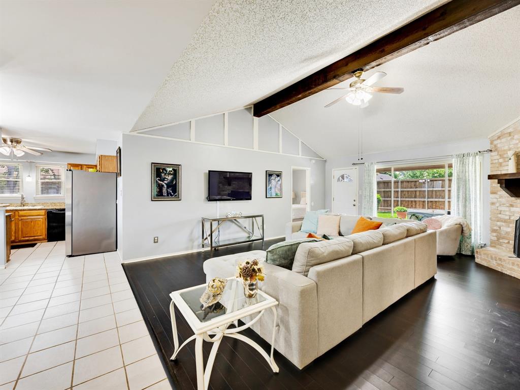 2032 Spicewood Road Bedford, TX 76021 - Photo 4 of 21 Expansive living area featuring vaulted ceilings with exposed wood beams, a stone-front fireplace with a wood mantle, and dark wood-finish flooring