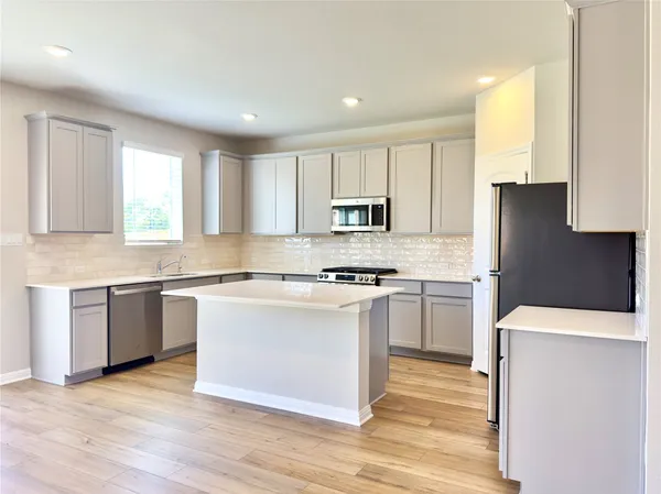 a kitchen with stainless steel appliances granite countertop a stove a sink dishwasher a refrigerator and white cabinets with wooden floor