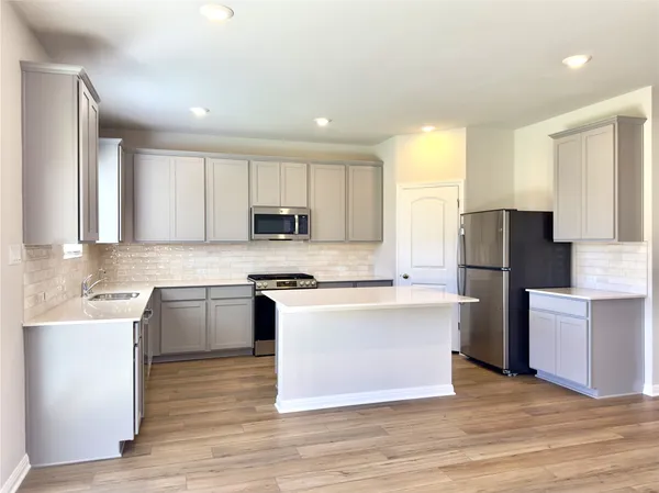 a kitchen with stainless steel appliances granite countertop a stove a sink a refrigerator white cabinets and wooden floor