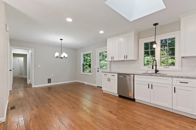 a kitchen with granite countertop a stove a sink and white cabinets with wooden floor