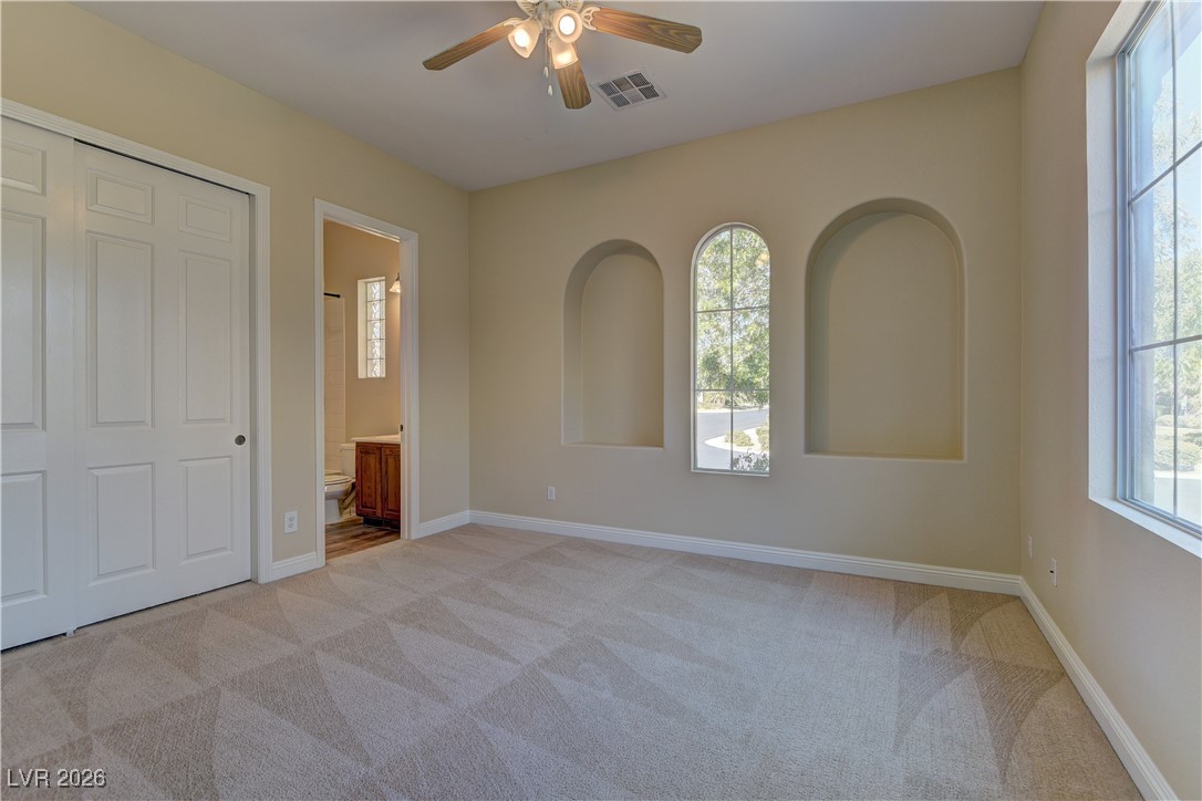 6383 Radiant Rapture Avenue Las Vegas, NV 89131 - Photo 12 of 17 Unfurnished bedroom with light colored carpet, multiple windows, ensuite bathroom, and ceiling fan