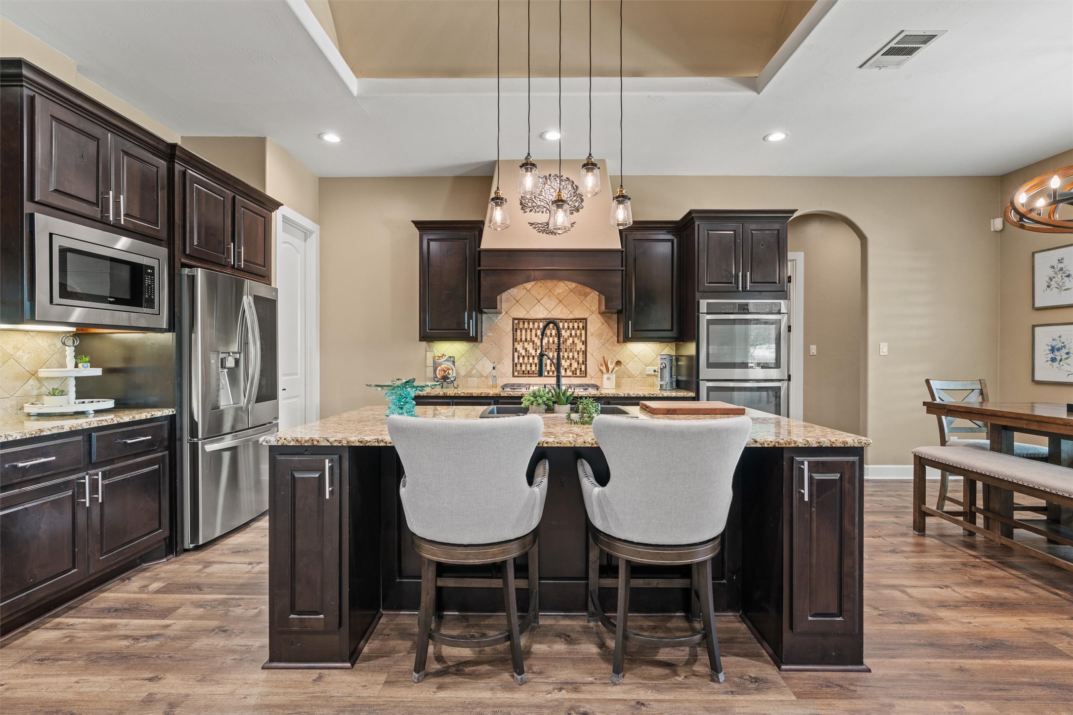 104 Adobe Cove Georgetown, TX 78633 - Photo 8 of 39 Kitchen with dark wood finish cabinetry, a center island with sink, arched walkways, light stone counters, and suspended lighting