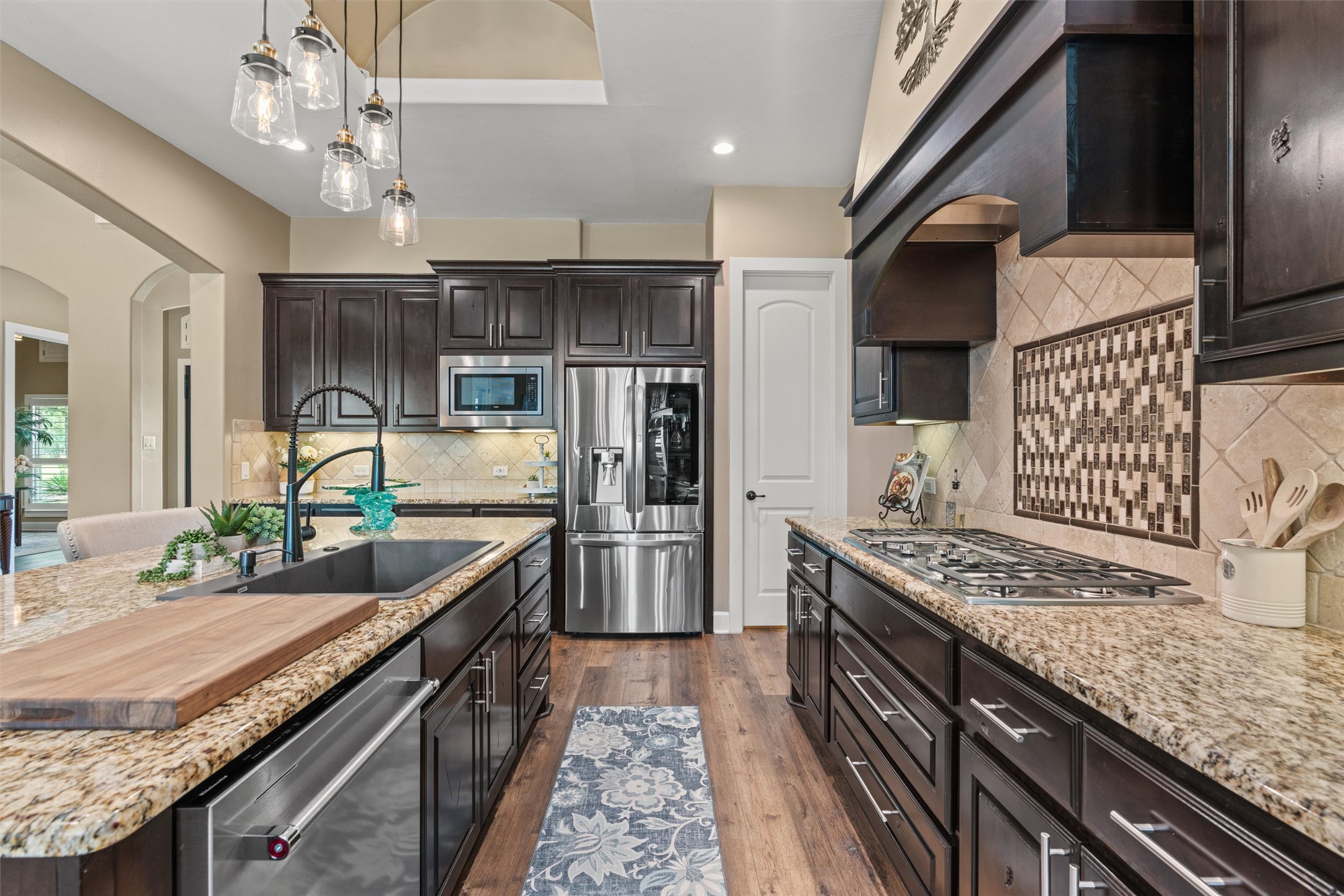 104 Adobe Cove Georgetown, TX 78633 - Photo 10 of 39 Kitchen featuring arched walkways, dark wood finish cabinetry, light stone counters, and stainless steel appliances