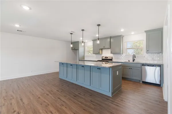 a kitchen with stainless steel appliances granite countertop a sink a stove a refrigerator and white cabinets with wooden floor