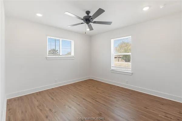 an empty room with wooden floor ceiling fan and windows