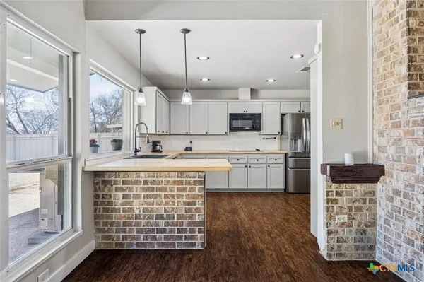a large kitchen with stainless steel appliances a stove a sink dishwasher a refrigerator white cabinets and wooden floor