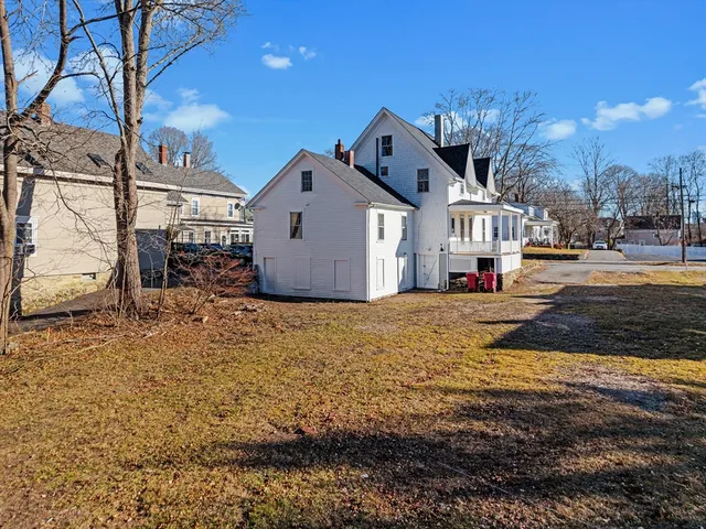 a view of a white house next to a yard with big trees