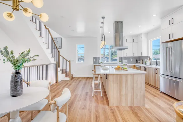 a kitchen with stainless steel appliances granite countertop a refrigerator a stove a sink dishwasher and a dining table with wooden floor