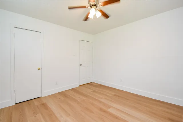 a view of an empty room with wooden floor and a ceiling fan