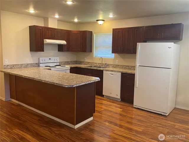 a kitchen with kitchen island granite countertop wooden cabinets a refrigerator a sink and a stove