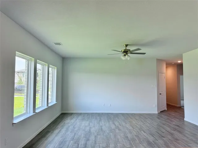 an empty room with wooden floor fan and windows