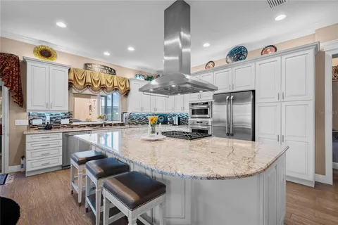 a kitchen with stainless steel appliances granite countertop a kitchen island a stove a sink a refrigerator and chairs