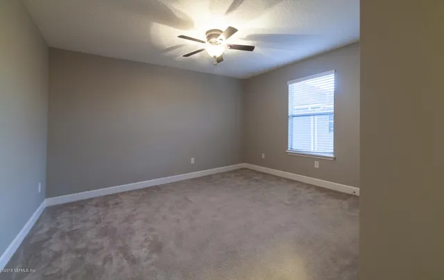 an empty room with chandelier fan and windows