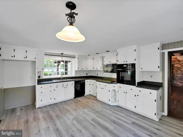 a kitchen with granite countertop a stove a sink and white cabinets with wooden floor