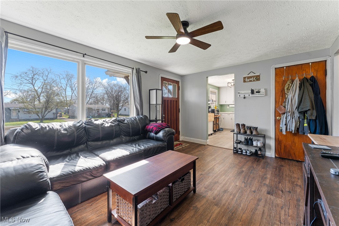 Living area featuring baseboards, a ceiling fan, wood finished floors, and a textured ceiling