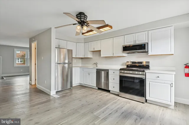 a kitchen with stainless steel appliances white cabinets a sink a stove a microwave and wooden floors