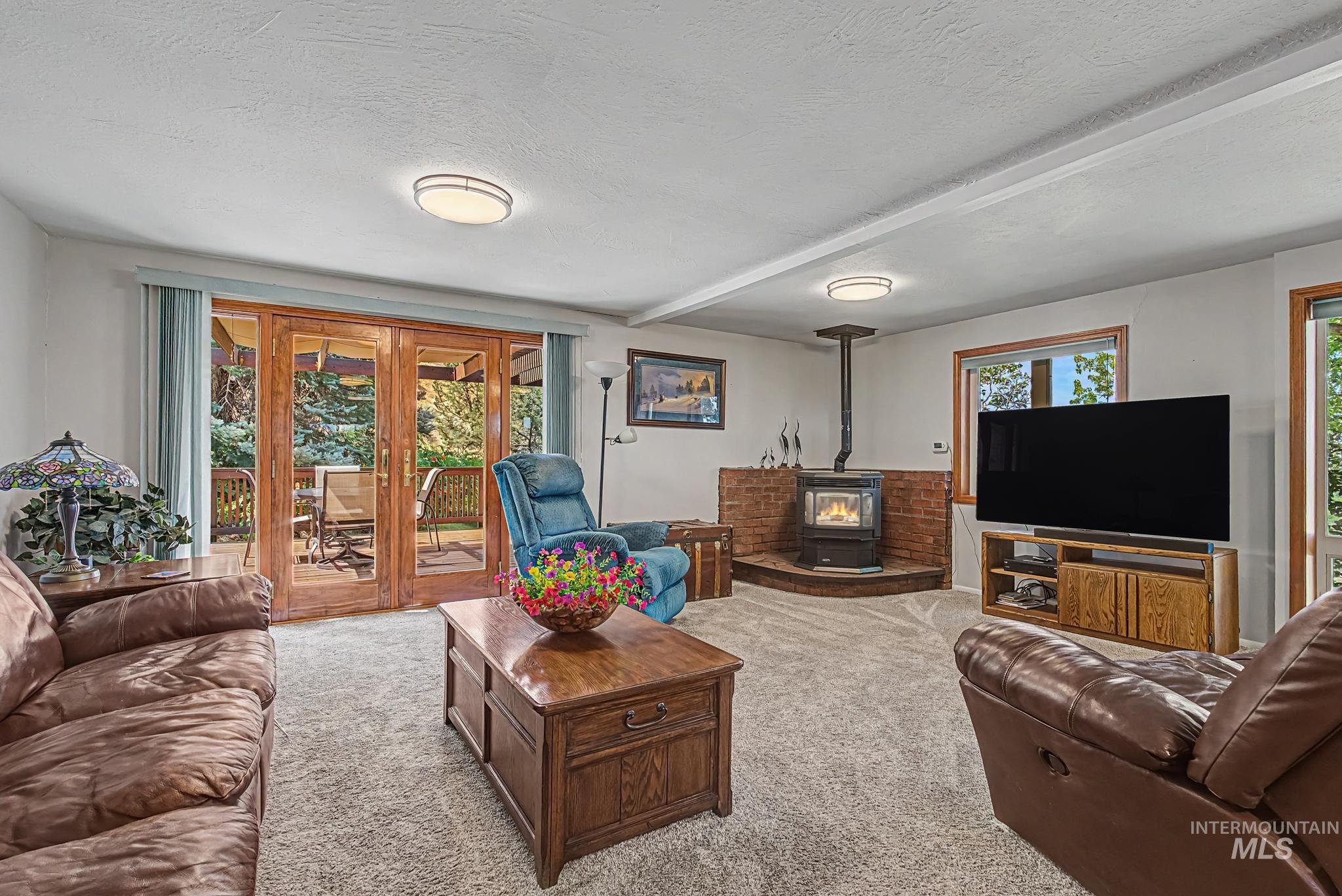 4311 Frozen Dog Road Emmett, ID 83617 - Photo 16 of 31 Living area featuring a wood-burning stove with a brick surround, light-toned carpet, and exposed ceiling beams