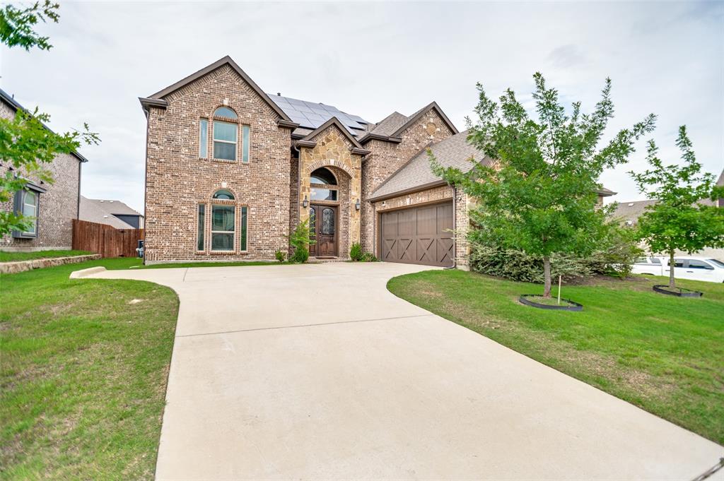 413 Frontier Court Midlothian, TX 76065 - Photo 1 of 26 Brick and stone exterior featuring arched window designs, a prominent arched entry, a two-car garage with wood-finish double doors, solar panels, and a concrete driveway