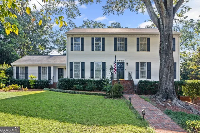 a view of a brick house with a yard plants and large tree