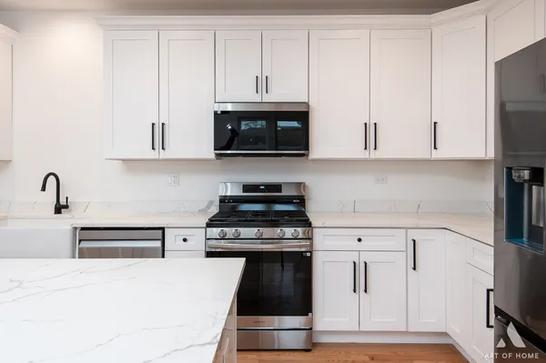 a kitchen with stainless steel appliances kitchen island granite countertop a stove a refrigerator a sink a microwave oven with white cabinets and wooden floor