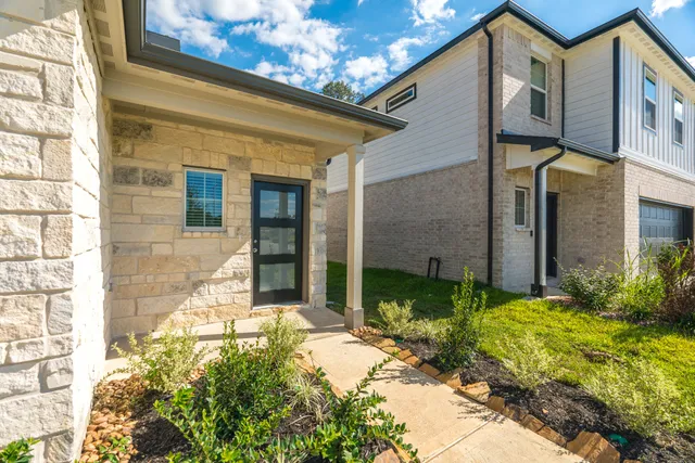 a view of a house with small yard plants and large tree