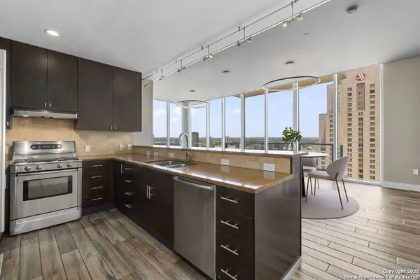 a kitchen with stainless steel appliances granite countertop a stove a sink dishwasher a microwave oven and a dining table with wooden floor