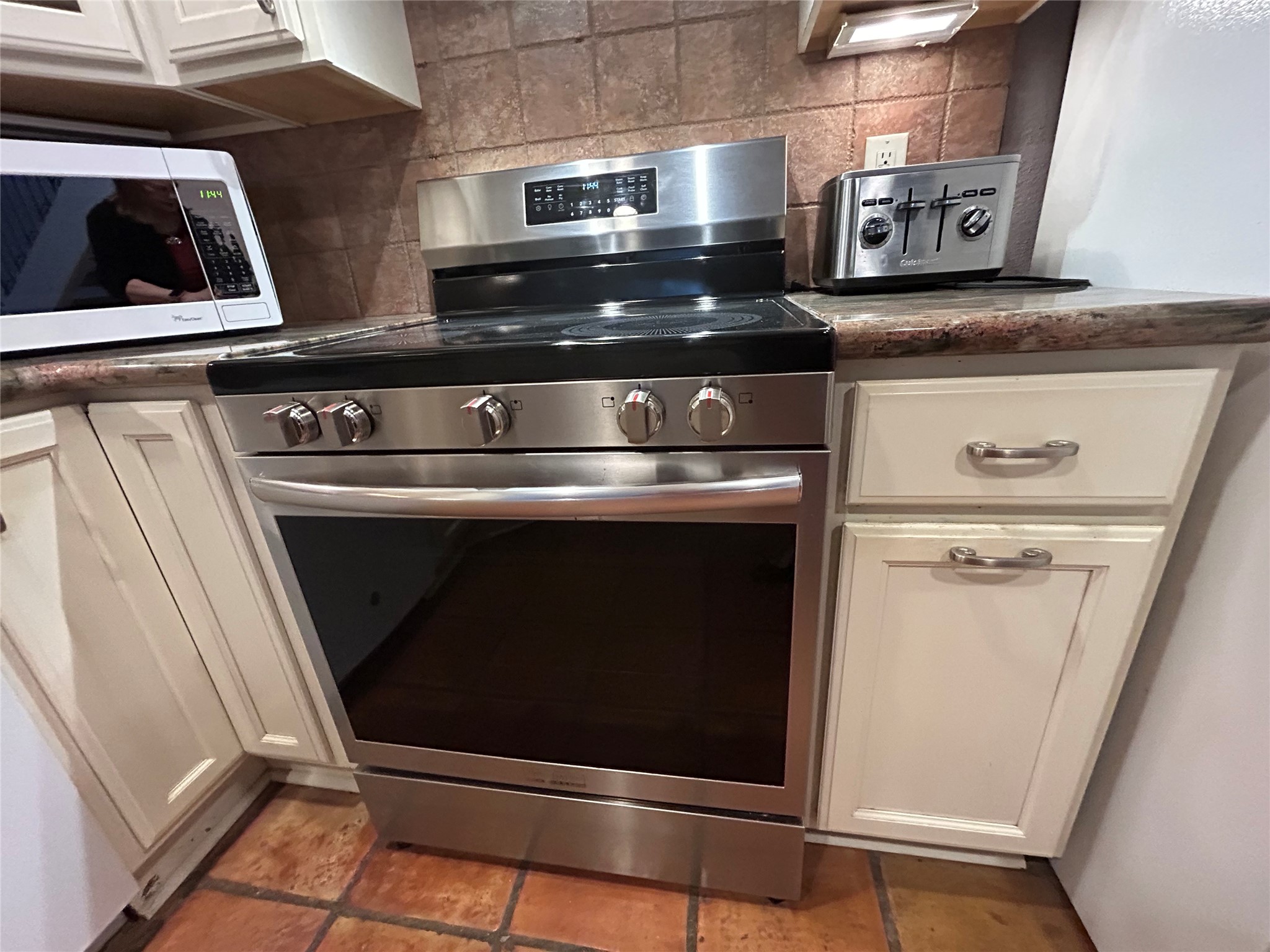 13034 Leader Street, Unit 965 Houston, TX 77072 - Photo 6 of 32 This kitchen features a modern stainless electric stove by Frigidaire Gallery with a sleek design, complemented by cream cabinetry and tiled flooring. The area is equipped with a microwave and toaster, providing functionality and convenience.