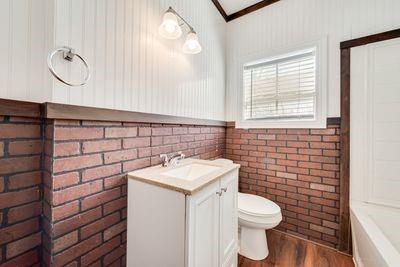 930 Freeman Street Sherman, TX 75092 - Photo 14 of 18 Bathroom featuring a white vanity with an integrated sink, a toilet, a window with blinds, and white beadboard paneling over brick-patterned wainscoting