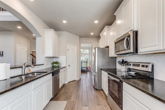 a kitchen with stainless steel appliances granite countertop a sink a stove top oven a refrigerator with wooden floors and cabinets