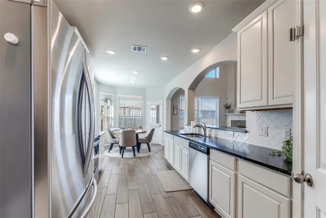a kitchen with sink a refrigerator and white cabinets with wooden floor