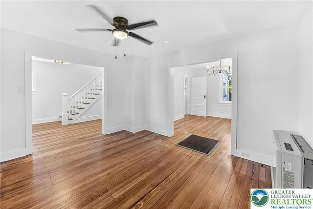 a view of an empty room with wooden floor and a ceiling fan
