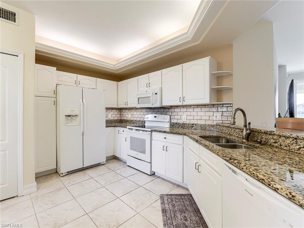 9040 Spring Run Boulevard, Unit 404 Estero, FL 34135 - Photo 11 of 34 a kitchen with granite countertop white cabinets and white appliances