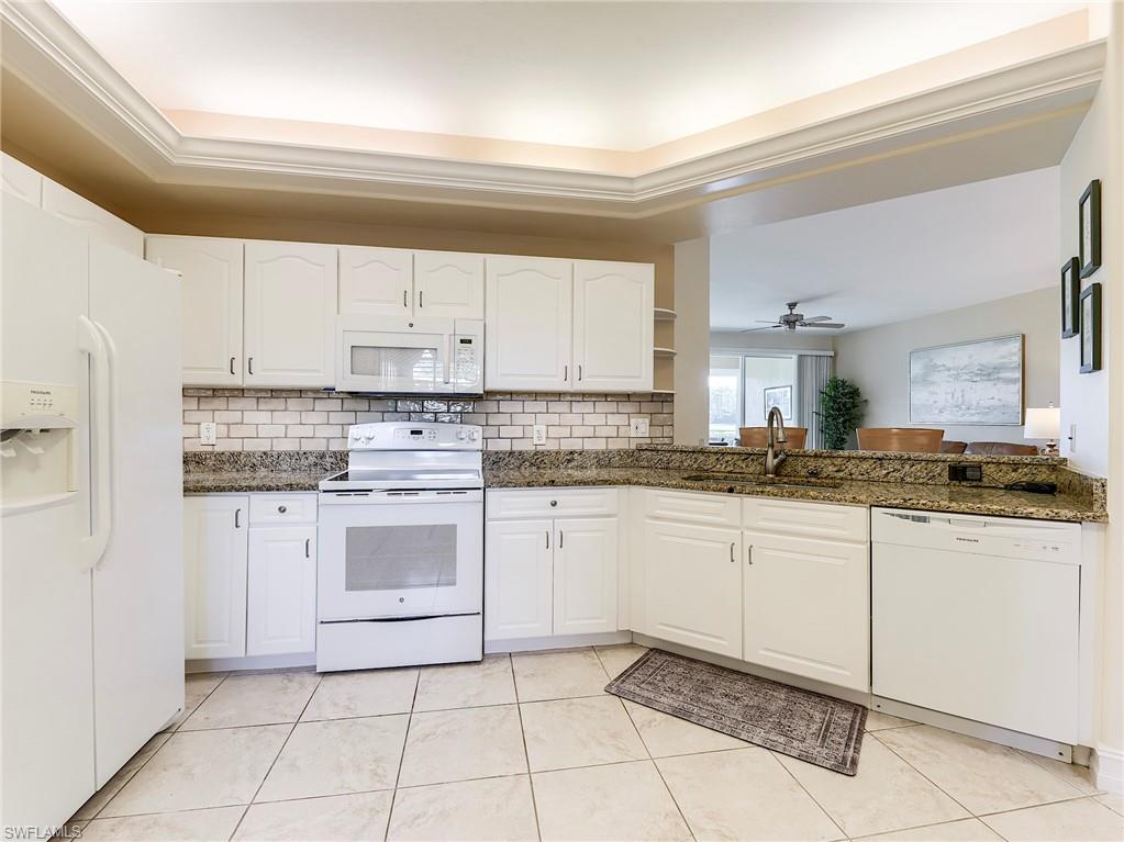 9040 Spring Run Boulevard, Unit 404 Estero, FL 34135 - Photo 12 of 34 a kitchen with granite countertop white cabinets and white appliances