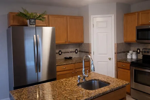a kitchen with stainless steel appliances granite countertop a refrigerator a stove and a sink with wooden floor