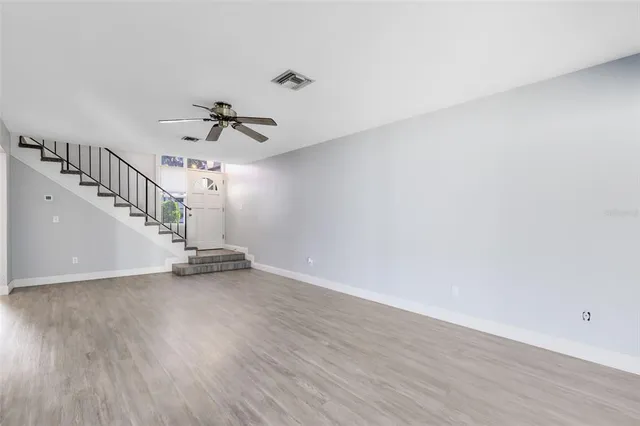 a view of an empty room with wooden floor and a ceiling fan