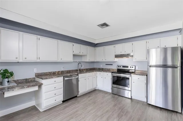 a kitchen with stainless steel appliances granite countertop a stove a sink dishwasher a refrigerator and white cabinets with wooden floor