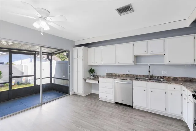 a kitchen with granite countertop a stove a sink a refrigerator and white cabinets with wooden floor