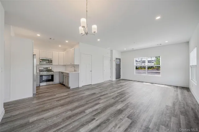 a view of an empty room and kitchen with wooden floor