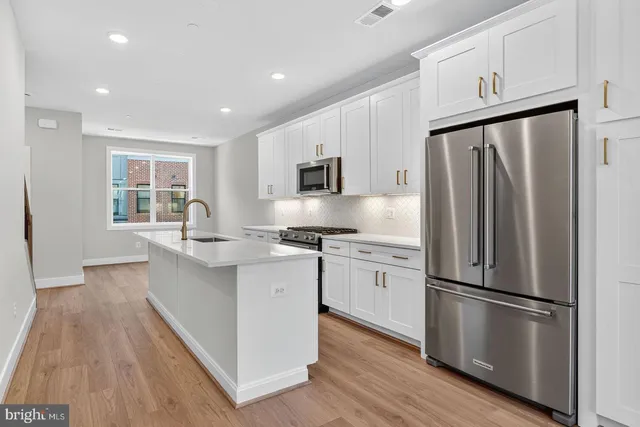 a kitchen with kitchen island granite countertop a refrigerator a sink dishwasher a stove and white cabinets with wooden floor