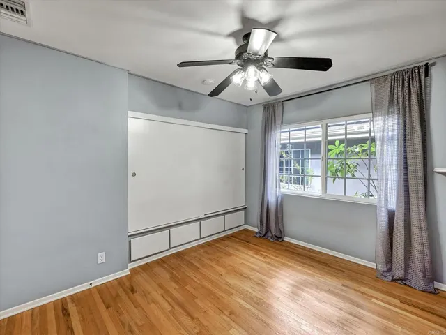 an empty room with wooden floor fan and windows