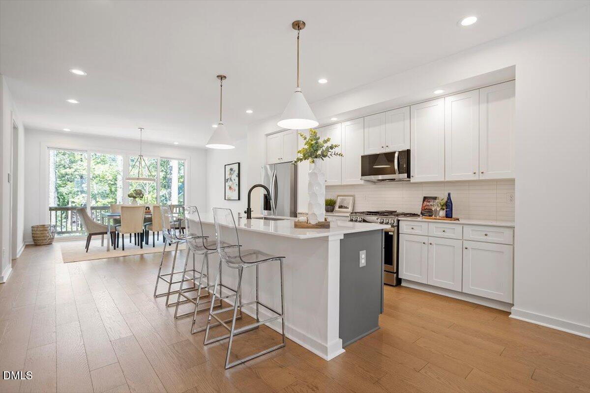 6419 Tanner Oak Lane Raleigh, NC 27613 - Photo 15 of 39 a kitchen with stainless steel appliances kitchen island granite countertop a stove top oven a sink a dining table and chairs with wooden floor