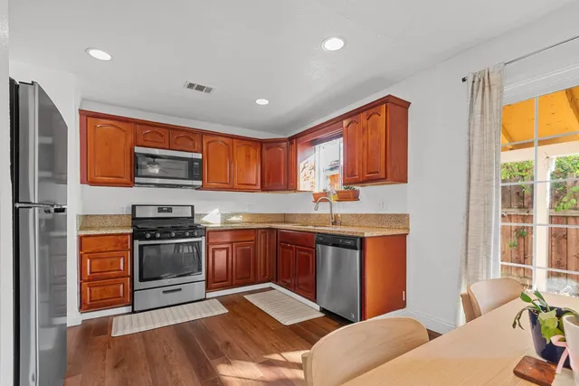 a kitchen with stainless steel appliances granite countertop a stove top oven a sink dishwasher a dining table and chairs with wooden floor