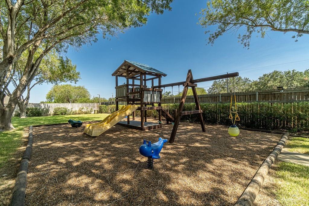 919 Hill Country Road Edinburg, TX 78539 - Photo 22 of 22 Playground area featuring a wooden playset with a slide and swings, surrounded by wood chip ground cover