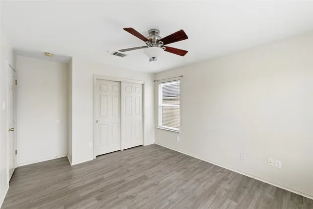 a view of an empty room with wooden floor and a ceiling fan