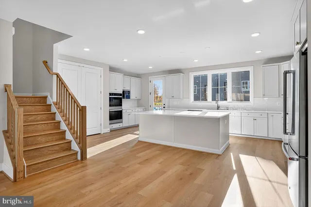a large white kitchen with kitchen island a large counter top a sink stainless steel appliances and cabinets