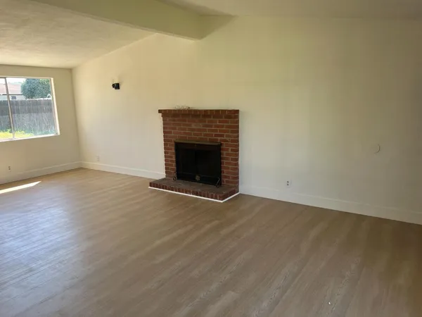 an empty room with wooden floor fireplace and windows