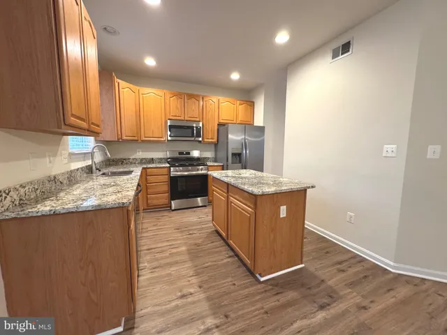 a large kitchen with stainless steel appliances granite countertop a stove a sink dishwasher and a refrigerator with wooden floor