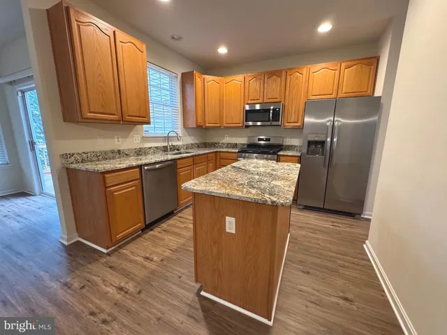 a kitchen with stainless steel appliances granite countertop wooden cabinets a stove a sink and dishwasher with wooden floor